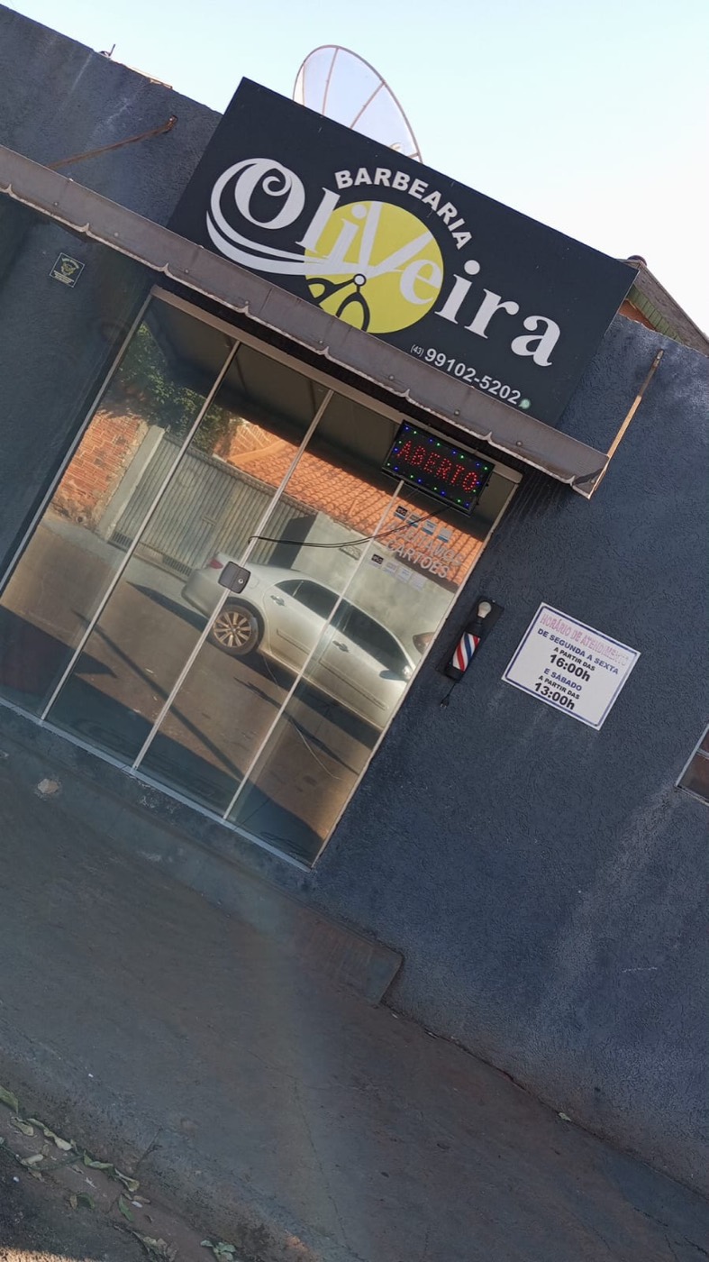 Fachada da Barbearia Oliveira: parede preta com letreiro dourado, vitrine de vidro e luminoso de aberto